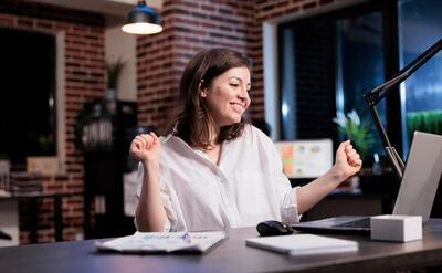 Happy joyful young adult businesswoman celebrating finishing startup project before deadline. enthusiastic positive young adult entrepreneur being excited about new job while in office at night.
