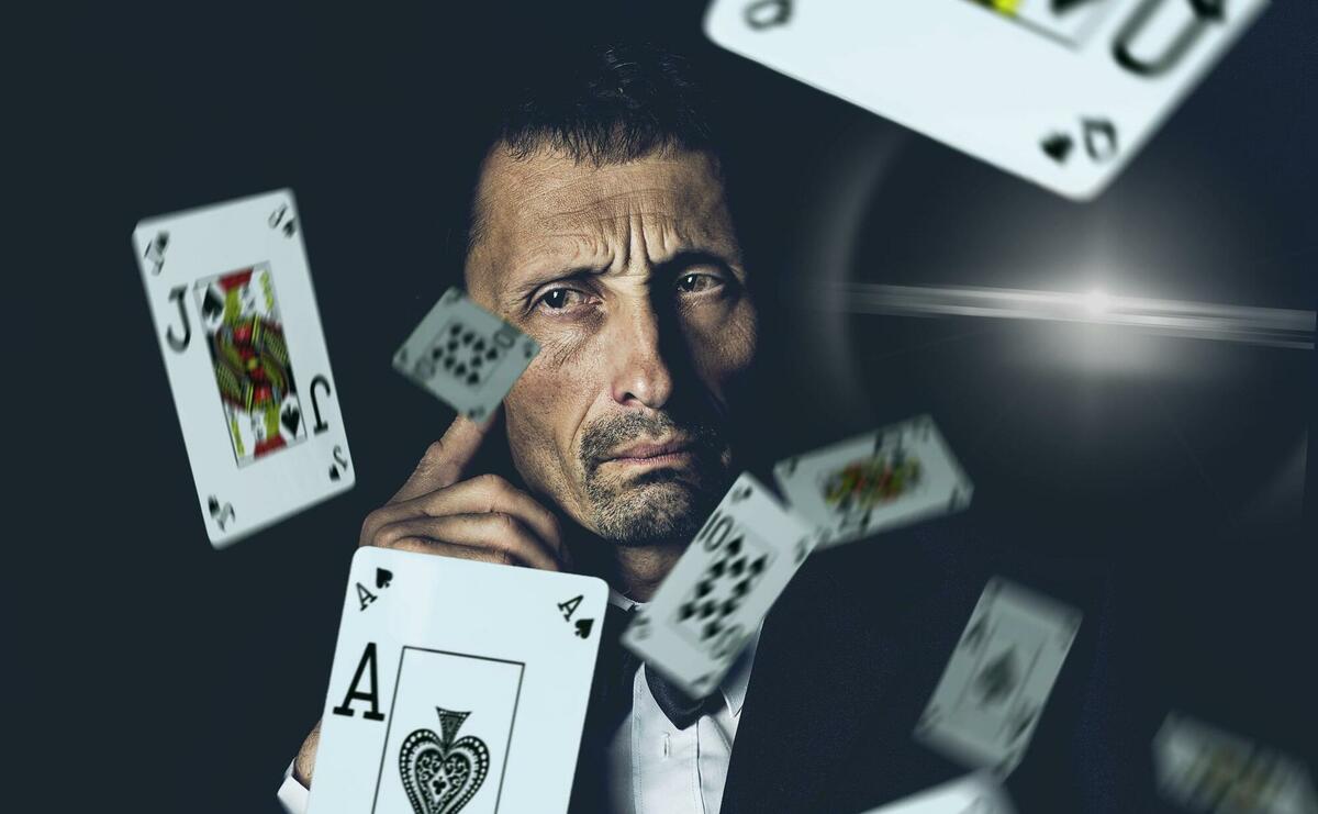 A person is thinking in the background, and playing cards are falling in the front.