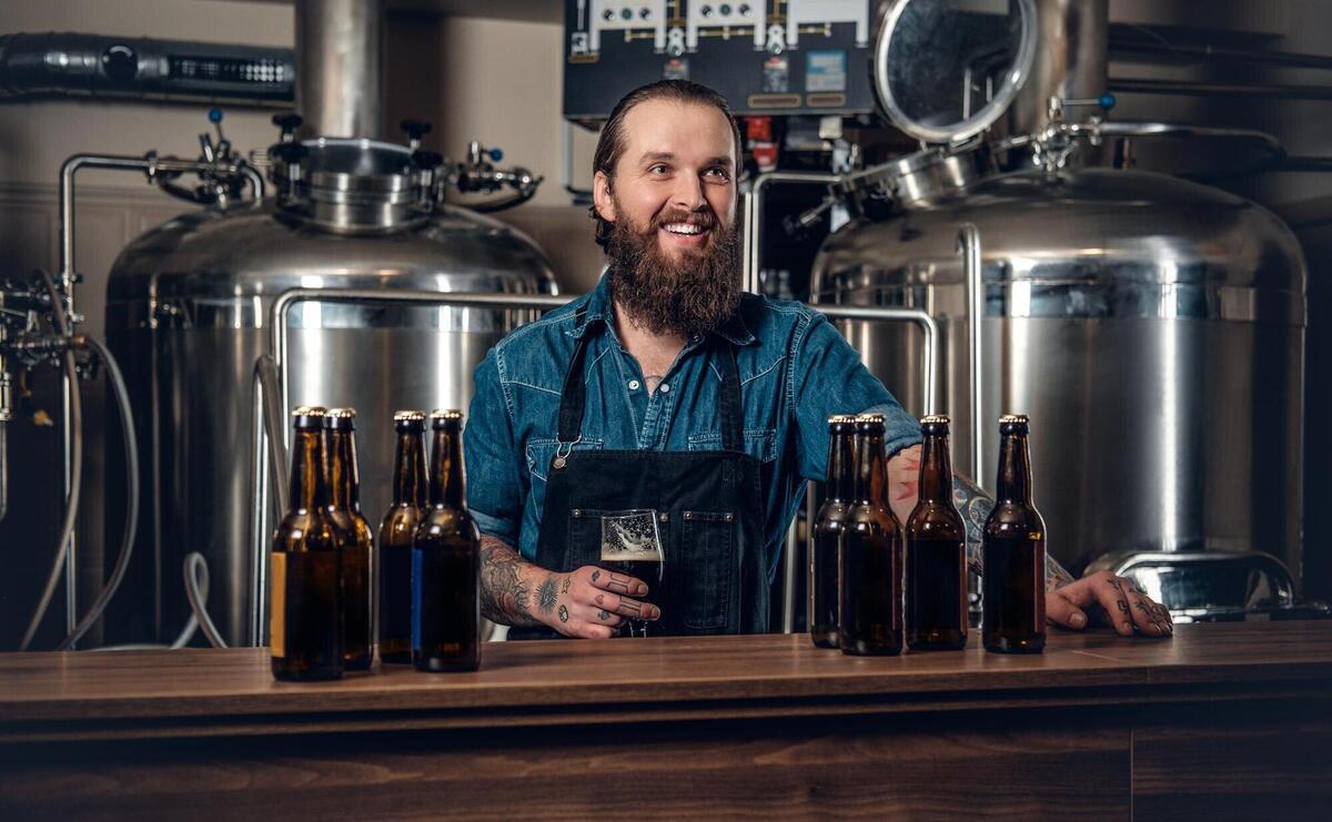 Portrait of tattooed, bearded hipster male manufacturer presenting beer microbrewery.