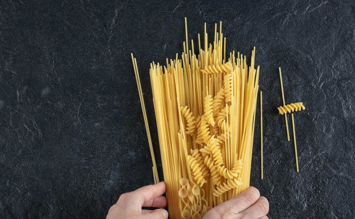Woman hands touching various pasta on dark surface.