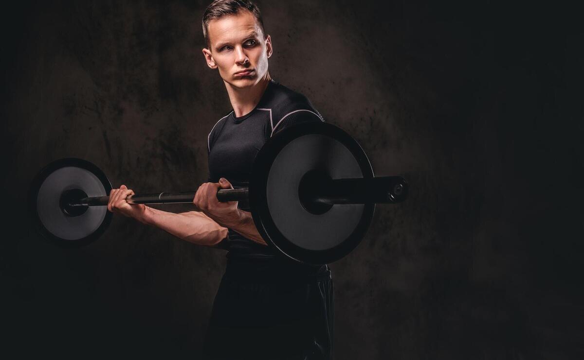 Focused young sportsman holding a barbell and doing exercise on biceps. isolated on a dark background.