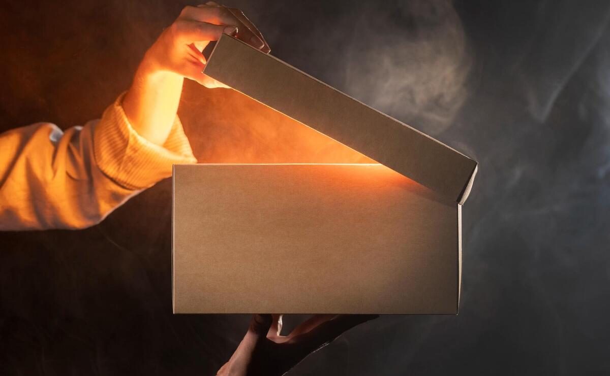 Hand opening a glowing box amidst mysterious smoke, revealing a radiant secret.