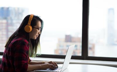 Woman with big yellow headphones is using laptop computer.