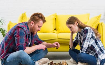 Side view of young couple sitting on white carpet playing the chess game