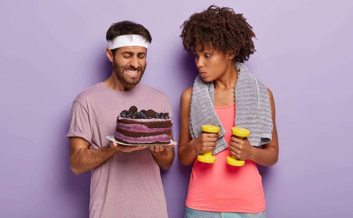 Young unshaven man holds plate of cake, clenches teeth, has temptation to eat dessert and surprised curly woman trains abs with dumbbells