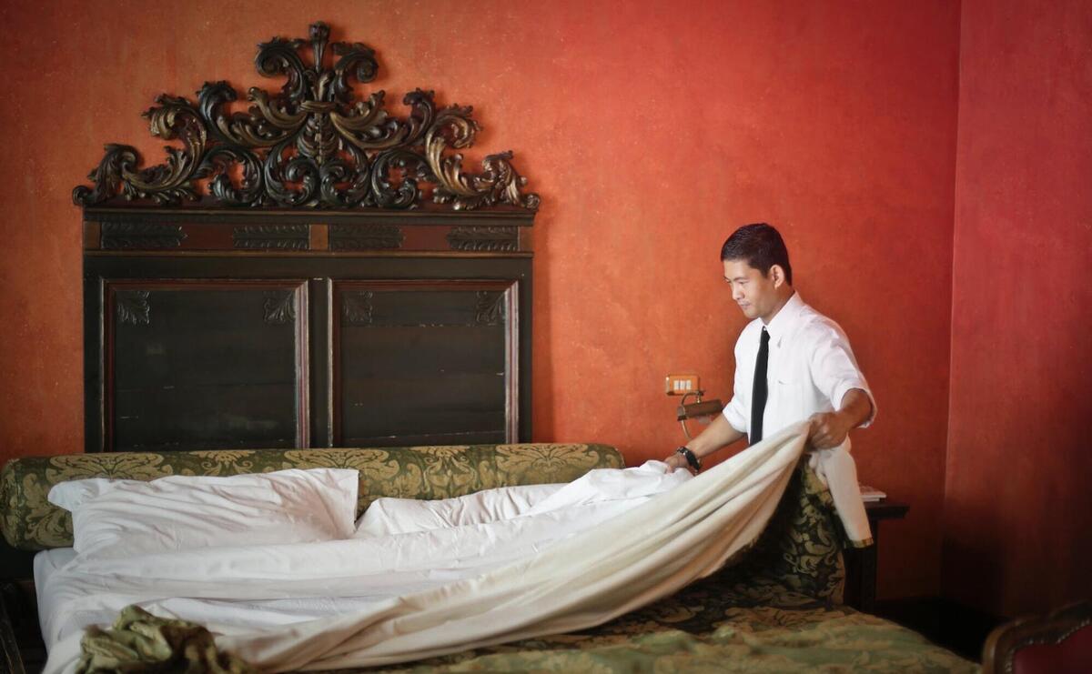 A cleaner is setting the bed in a hotel.