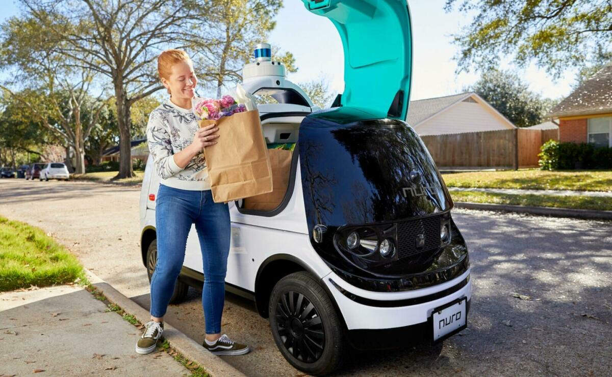 A child is unloading groceries from a small electronic vehicle.