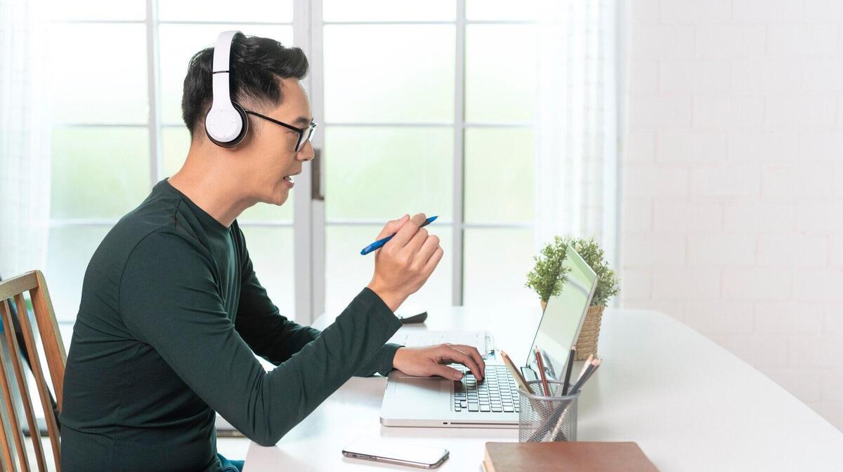 Smiling handsome asian businessman wear headphones working remotely from home. he is webinar video conference