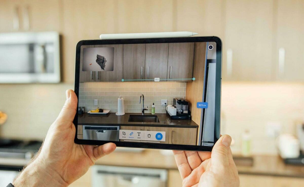 A user is holding a tablet in the kitchen, the camera recording the view and adds interactive controls to objects.