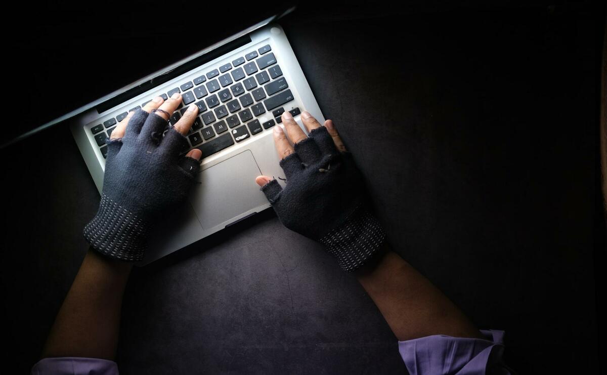 A hand with thief gloves using a laptop.