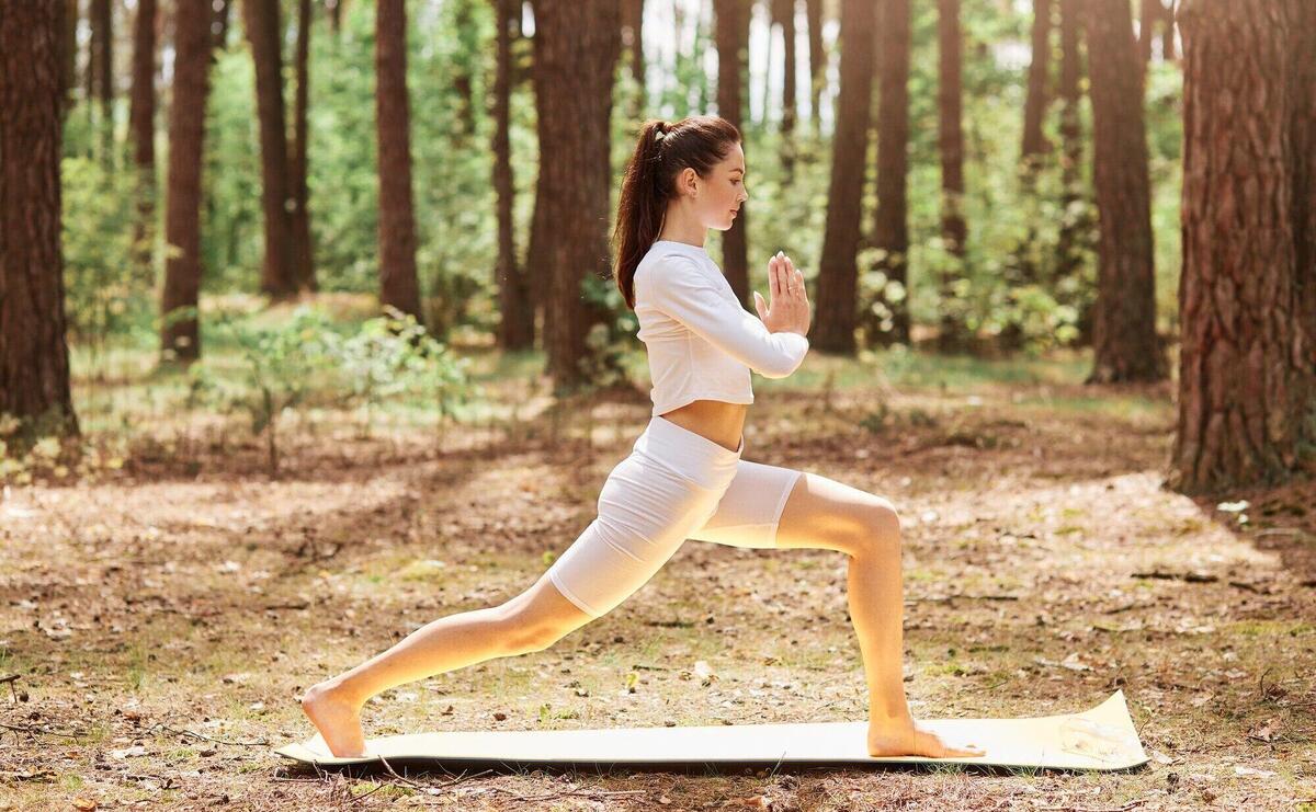 Profile full length photo of young adult woman with ponytail dresses white stylish sportswear doing yoga outdoors, pressing palms together, meditation and relaxing.
