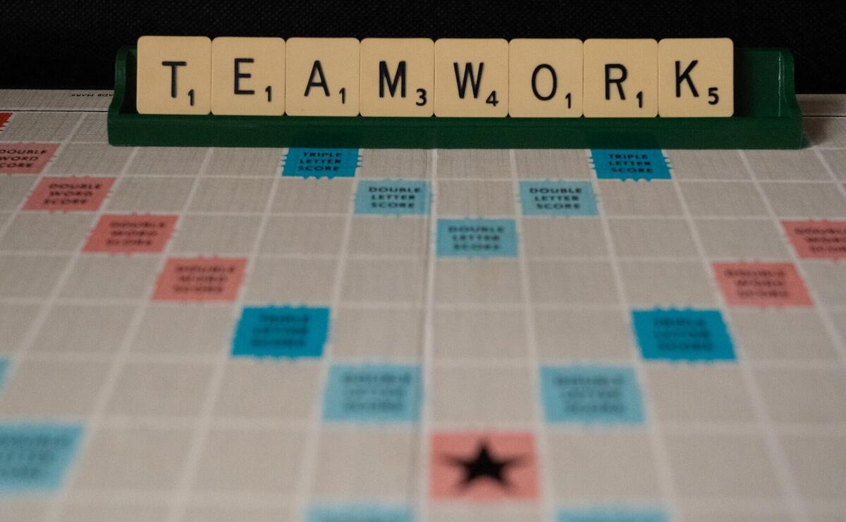 A scrabble game board with a tile rack holding the letters spelling out TEAMWORK.