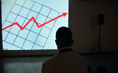 Man wearing white top looking at projector graph screen.