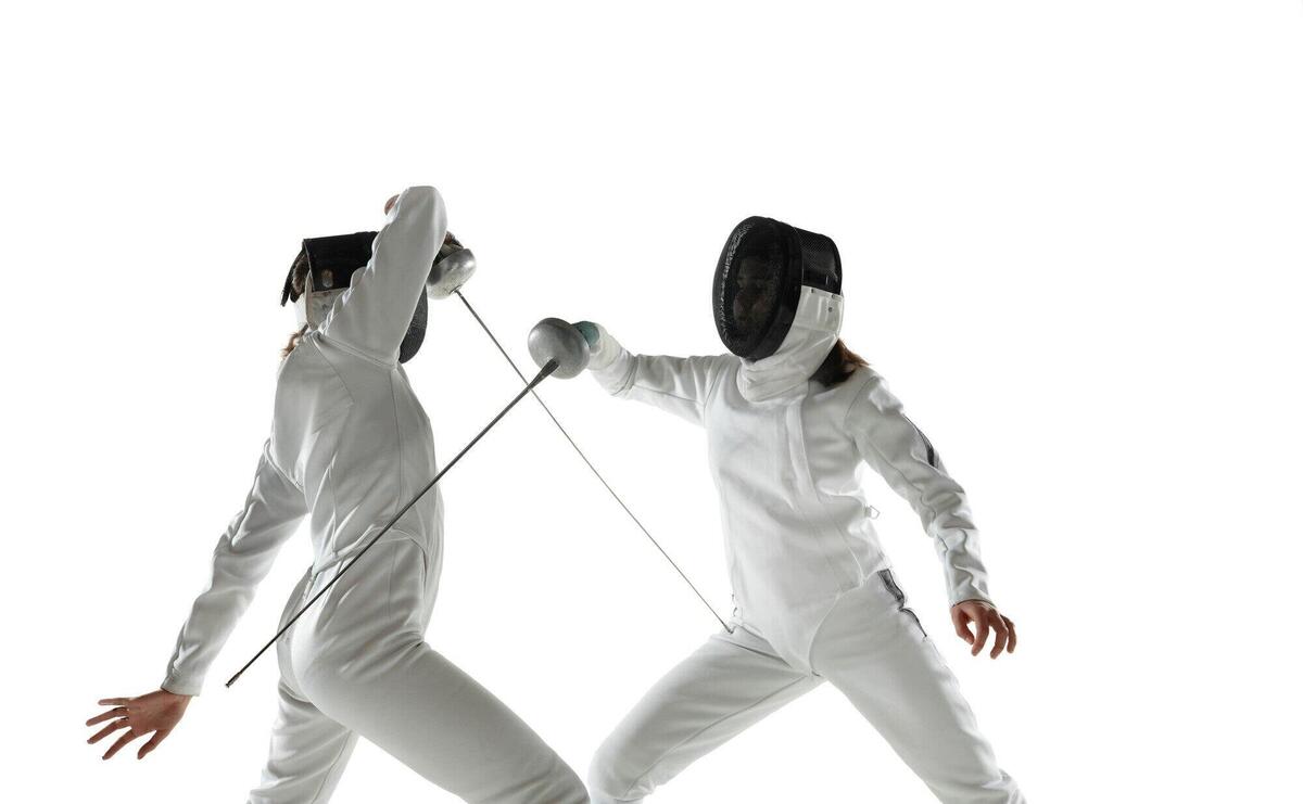 Teen girls in fencing costumes with swords in hands isolated on white studio background. young female models practicing and training in motion, action. copyspace. sport, youth, healthy lifestyle.