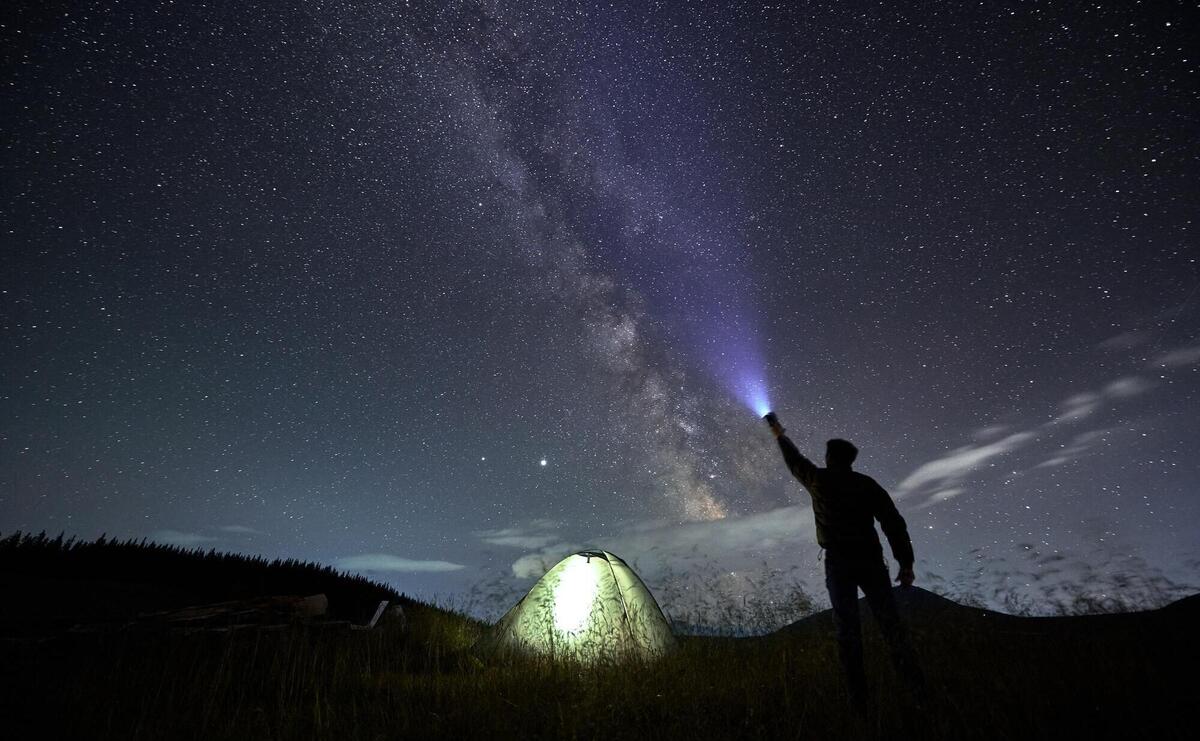 Male traveler shining flashlight into night starry sky
