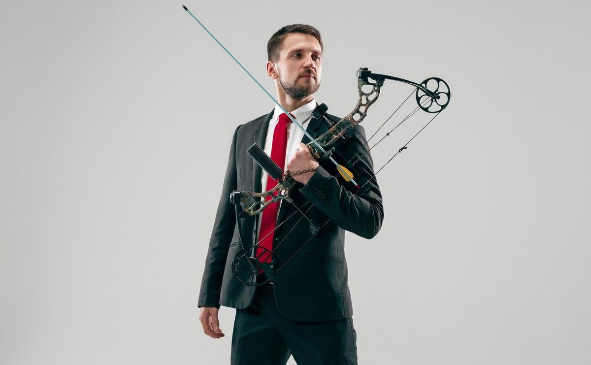 Businessman aiming at target with bow and arrow isolated on gray studio background. the business, goal, challenge, competition, achievement, purpose, victory, win, clarity, winner and success concept