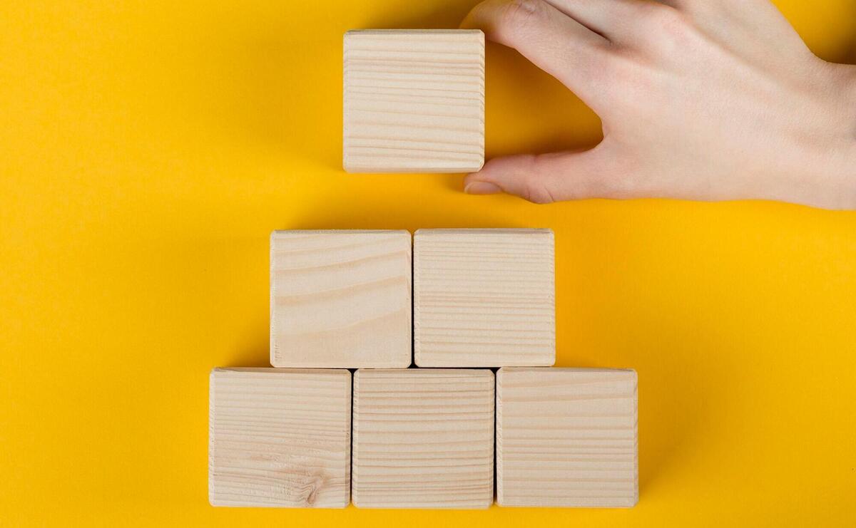 Hand positioning wooden blocks on a bright yellow background.
