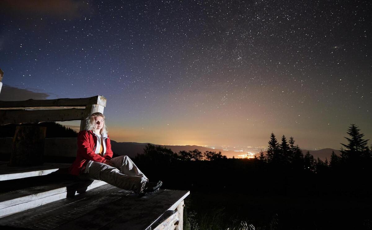 Beautiful young woman sitting under night starry sky.
